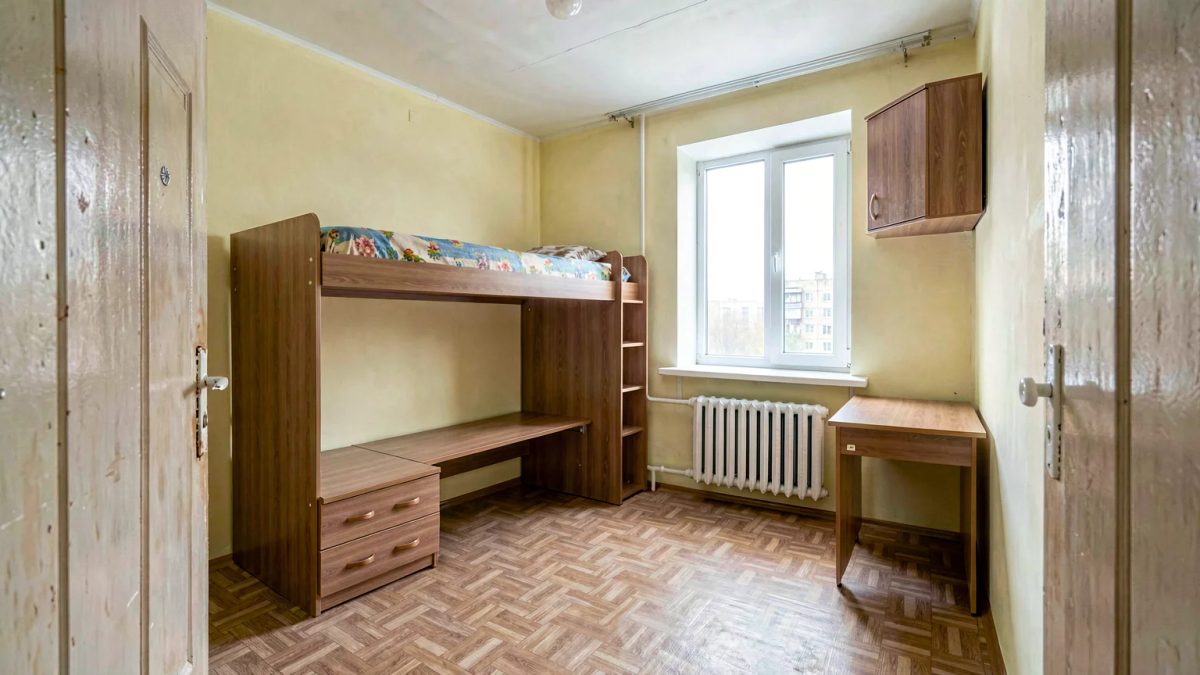 Детская 9 м² в хрущёвке: кровать средней высоты с ящиками и выдвижным столом внизу, шкафчик над дверью, светло-жёлтые стены, низкий потолок