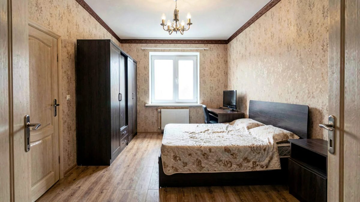 Спальня 10 м² до ремонта: массивный тёмный шкаф у двери, кровать посреди комнаты, стол с монитором втиснут у окна
