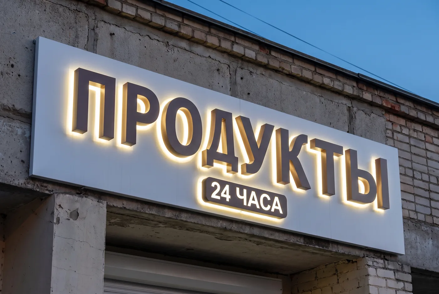 Подсвеченная вывеска ПРОДУКТЫ — фасад продуктового магазина крупным планом
